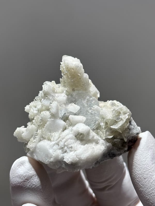 White feldspar cluster with aquamarine, mica and quartz from Xuebaoding, Sichuan, China, held in gloved hand