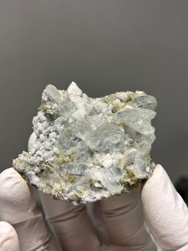 Pale aquamarine cluster over white feldspar and mica from Xuebaoding, Sichuan, China, held in gloved hand