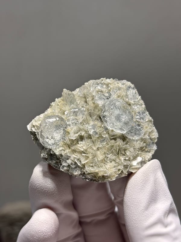 Aquamarine plate on mica from Xuebaoding, Sichuan, China, held in gloved hand