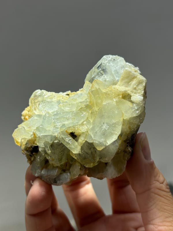 Yellow-green aquamarine crystals with cassiterite and feldspar from Xuebaoding, Sichuan, China, held in hand