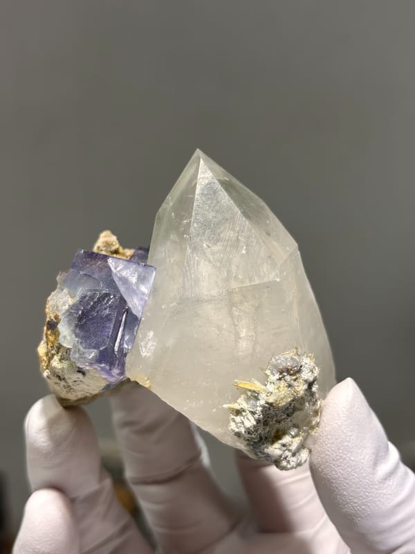 Clear quartz point with purple fluorite cube from Yaogangxian, Hunan, China, held in gloved hand