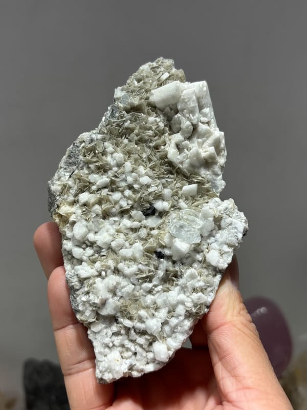 Plate of mica and feldspar with aquamarine and cassiterite from Xuebaoding, Sichuan, China, held in hand
