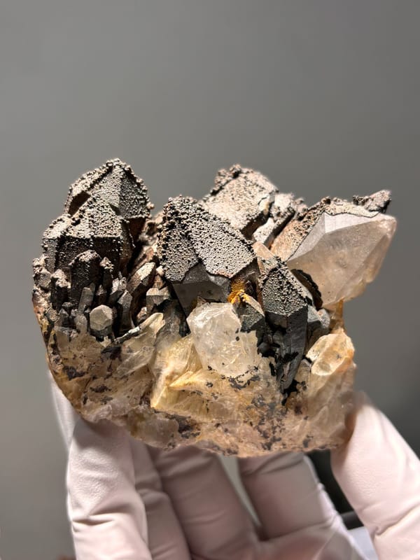 Madagascan quartz cluster with hematite-coated tips, held in gloved hand