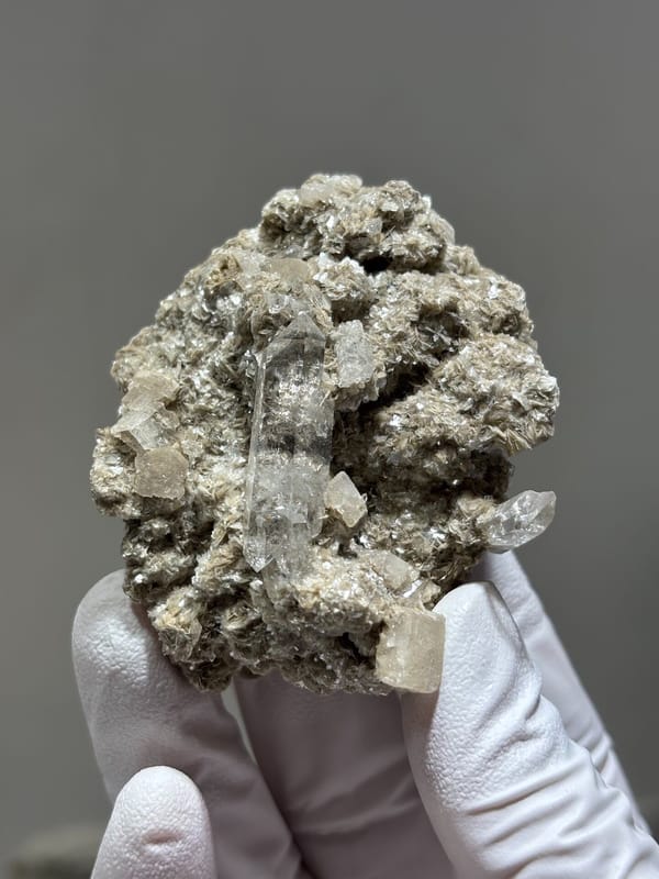 Clear quartz point in mica and calcite matrix from Xuebaoding, Sichuan, China, held in gloved hand