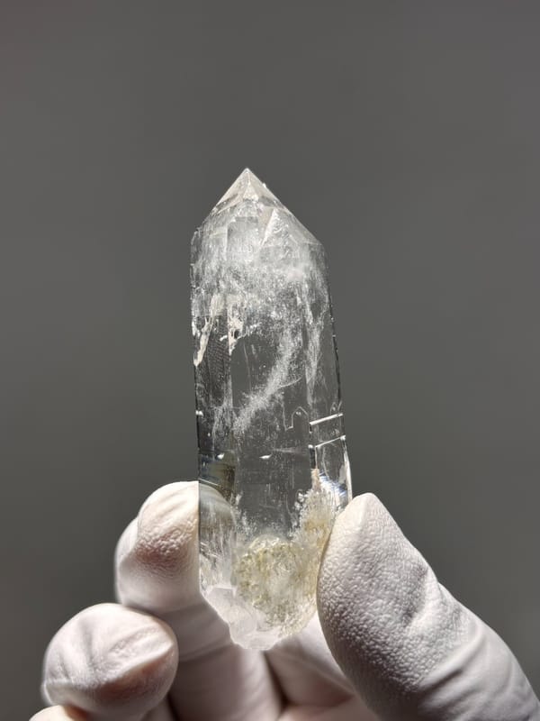 Bright clear quartz point with chlorite base from Xuebaoding, Sichuan, China, held in gloved hand