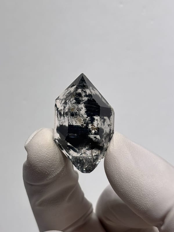 Scattered-ink double-terminated quartz from Chongqing, China, held in gloved hand