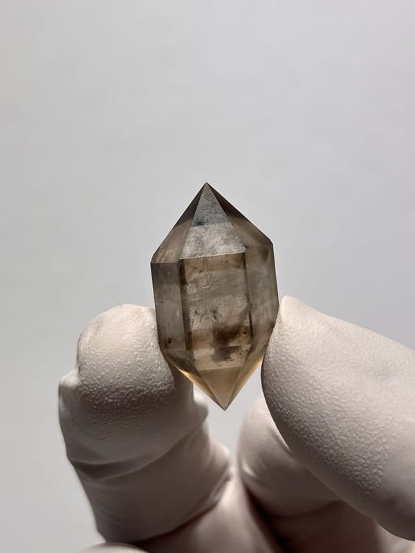 Tiny smoky double-terminated quartz with phantom from Yunnan, China, held in gloved hand