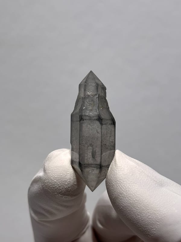 Grey sketch-pattern double-terminated quartz with sceptre tip from Yunnan, China, held in gloved hand