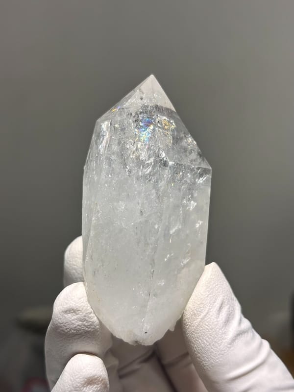 Icy clear quartz point with rainbow flash from Jinkouhe, Sichuan, China, held in gloved hand