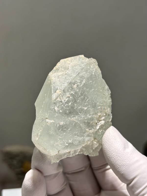 Frosted pale aquamarine tablet from Xuebaoding, Sichuan, China, held in gloved hand