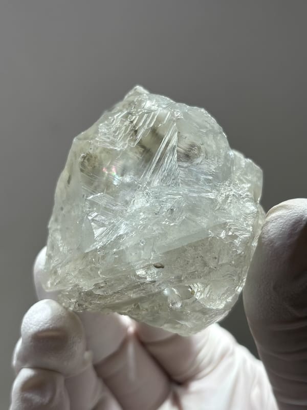 Colourless fluorite octahedron from Xuebaoding, Sichuan, China, held in gloved hand