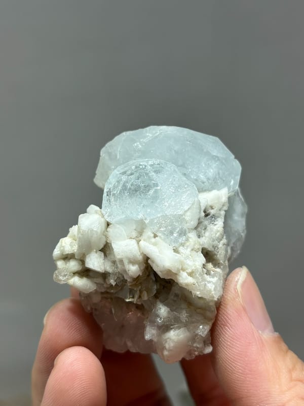 Pale blue aquamarine on white feldspar and mica from Xuebaoding, Sichuan, China, held in hand