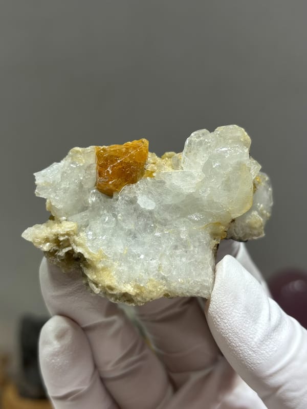 Pale aquamarine cluster with orange scheelite crystal from Xuebaoding, Sichuan, China, held in gloved hand