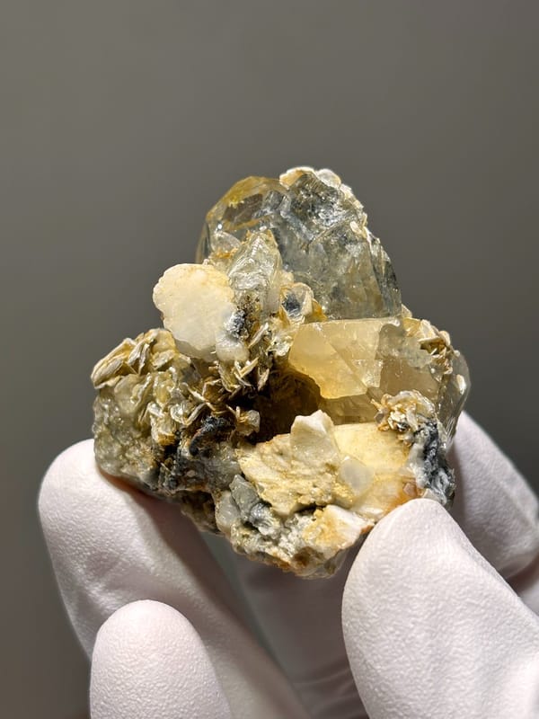 Aquamarine cluster with mica, scheelite and feldspar from Xuebaoding, Sichuan, China, held in gloved hand