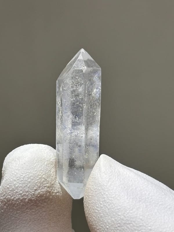 Tiny dumortierite-in-quartz double-terminated crystal from Brazil, held in gloved hand