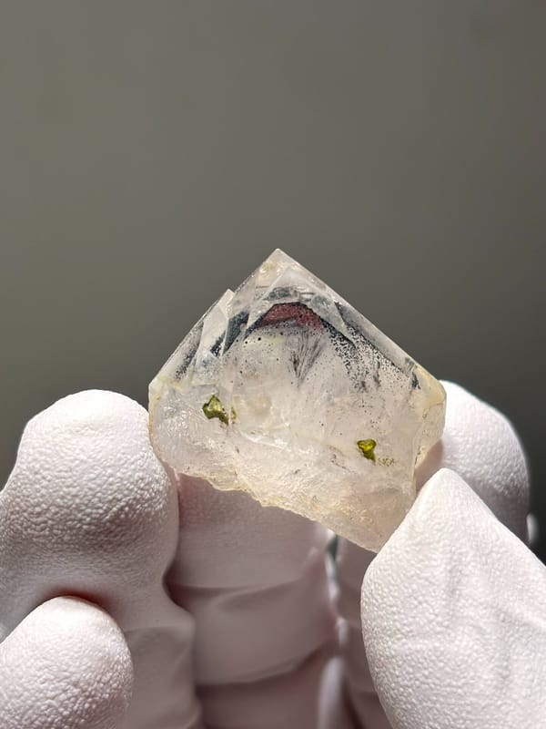 Tiny garden quartz with green epidote specks from Sichuan, China, held in gloved hand