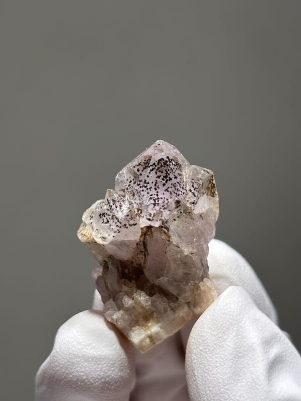 Garden quartz with black specks and pink tint from Sichuan, China, held in gloved hand