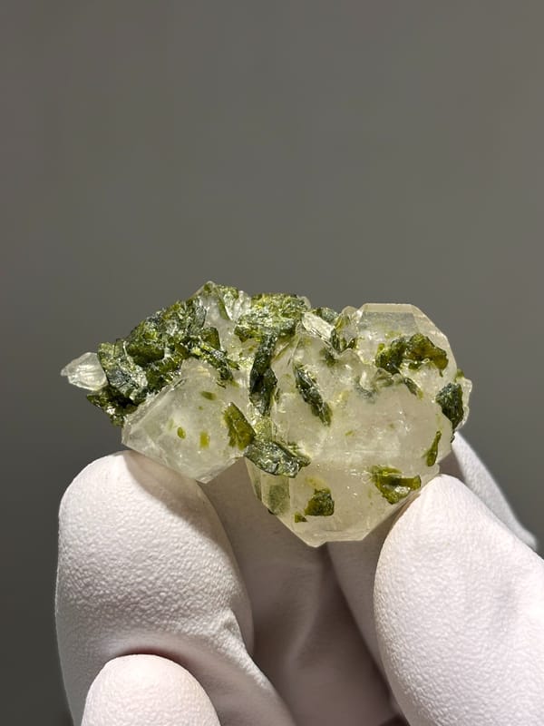 Flat garden quartz with green epidote sprays from Sichuan, China, held in gloved hand