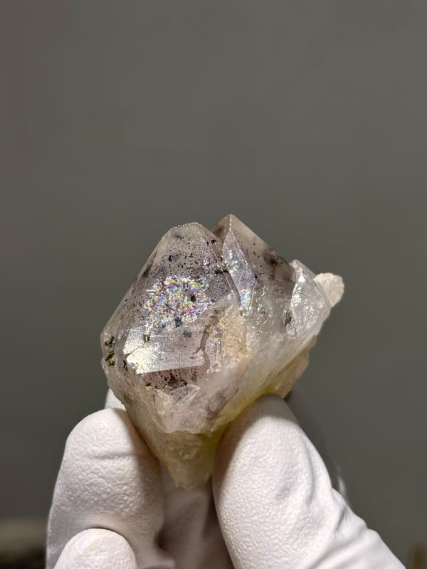 Garden quartz with dark inclusions and rainbow flash from Sichuan, China, held in gloved hand