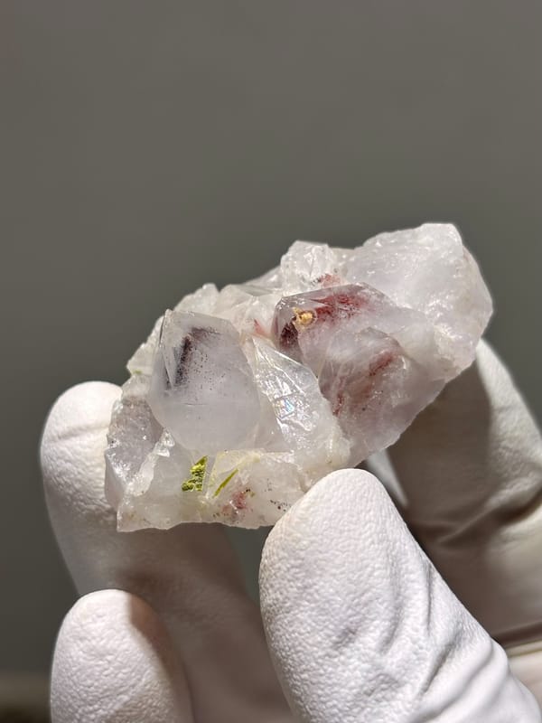 Garden quartz cluster with red and green inclusions from Sichuan, China, held in gloved hand