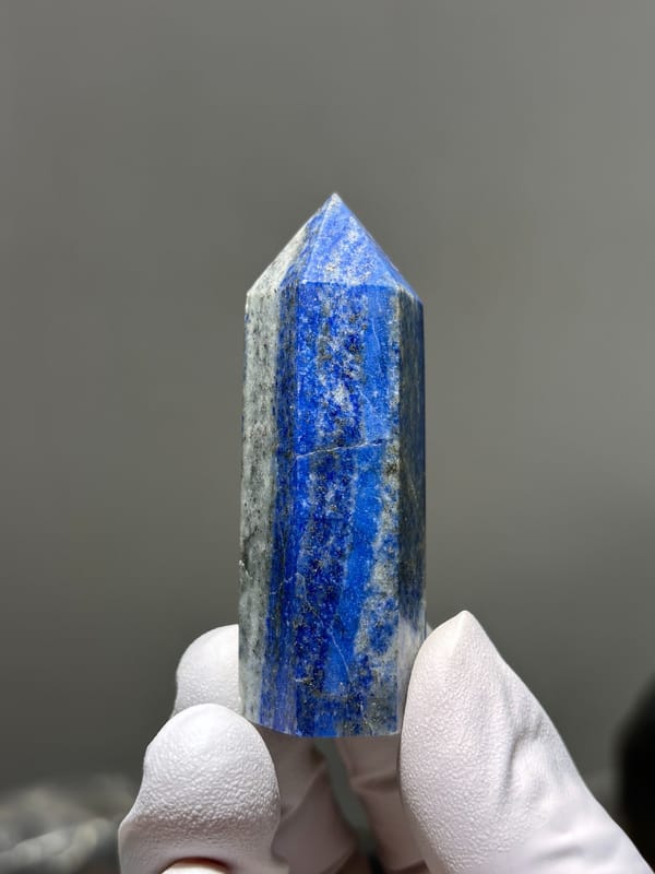 Polished lapis lazuli point with pyrite flecks from Afghanistan, held in gloved hand