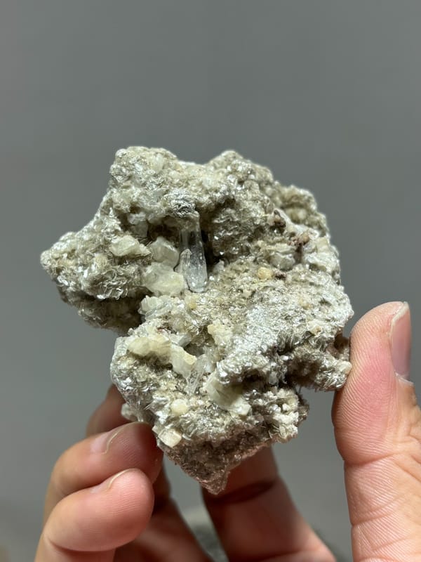 Silvery mica block with small quartz prism and white calcite from Xuebaoding, Sichuan, China, held in hand