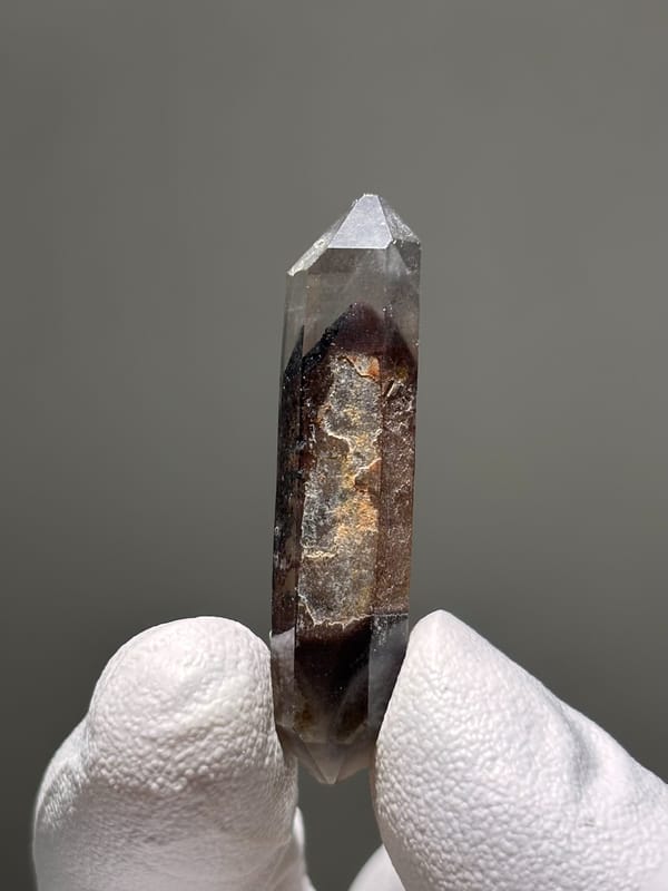 Slender red phantom quartz wand from Brazil, held in gloved hand