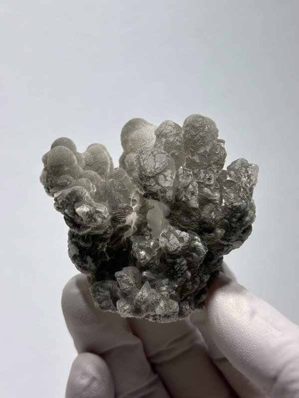 Grey botryoidal hydrozincite cluster from Yunnan, China, held in gloved hand