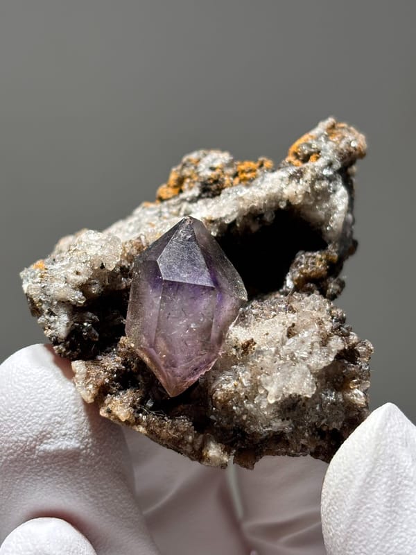 Purple amethyst point on druse matrix from Zimbabwe, held in gloved hand