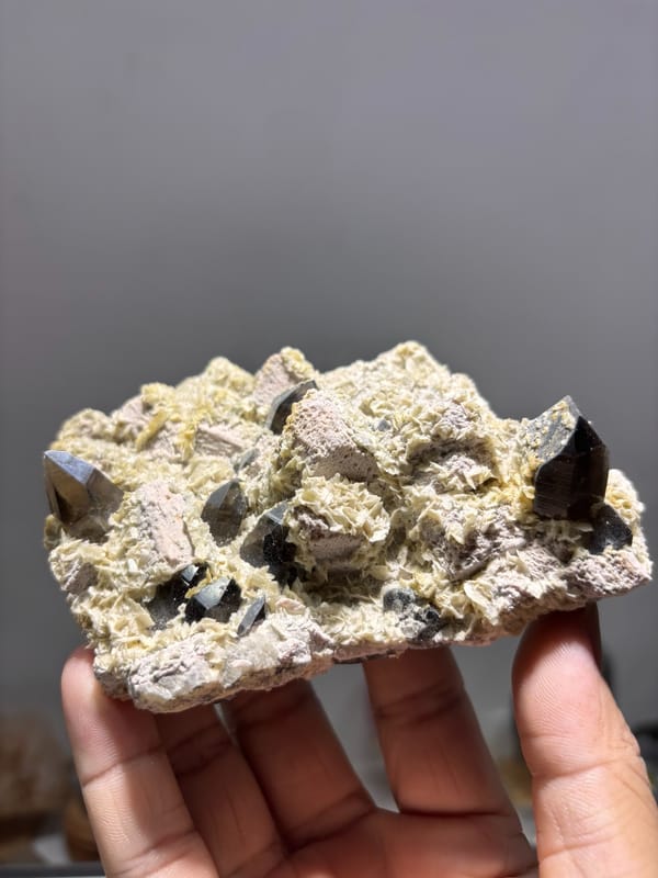 Feldspar plate with smoky quartz and calcite from Fujian, China, held in hand