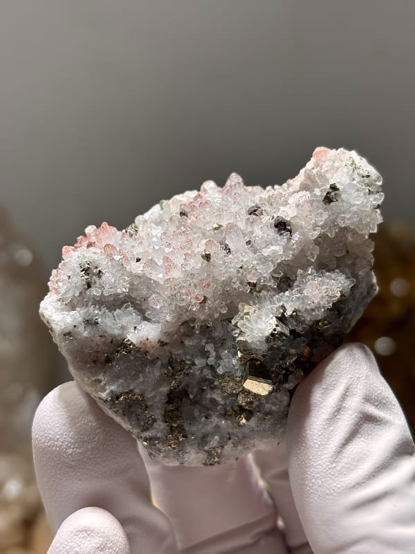Pink-skinned quartz druse with pyrite from Jiangxi, China, held in gloved hand