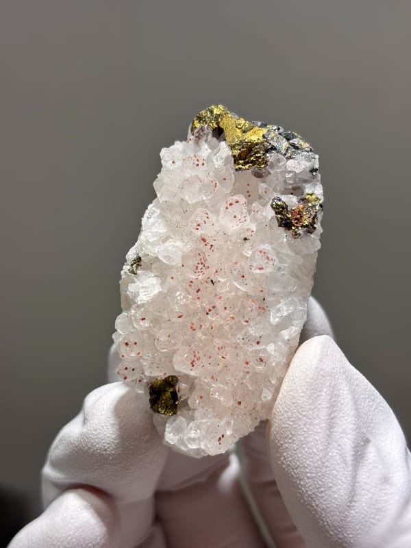 White quartz plate with red specks and chalcopyrite from Jiangxi, China, held in gloved hand