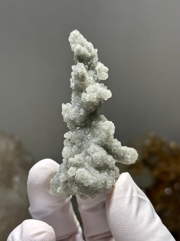 Grey-green botryoidal apophyllite spire over quartz from Hubei, China, held in gloved hand