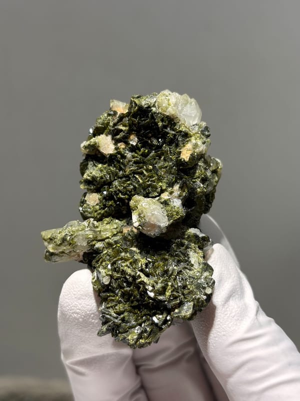 Dark green epidote cluster with white quartz points from Sichuan, China, held in gloved hand