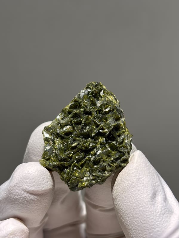 Dark green epidote crystal cluster from Sichuan, China, held in gloved hand