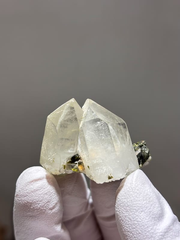 Two clear quartz points with green epidote from Sichuan, China, held in gloved hand