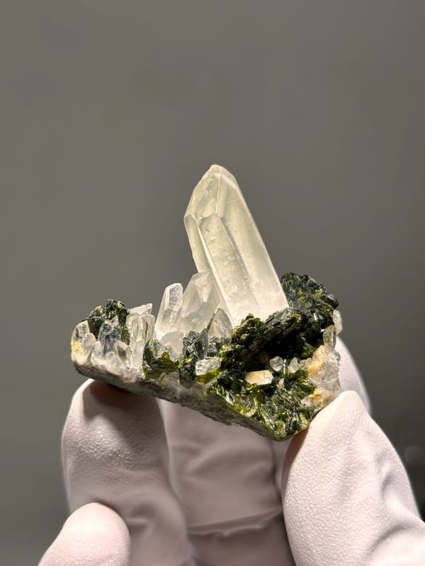 Milky quartz point on green epidote from Sichuan, China, held in gloved hand