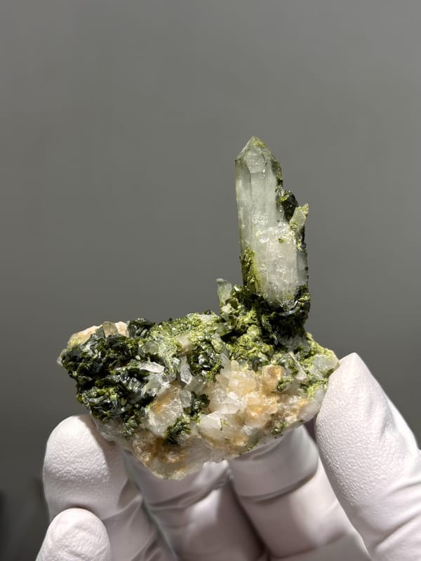 Clear quartz point rising from green epidote from Sichuan, China, held in gloved hand