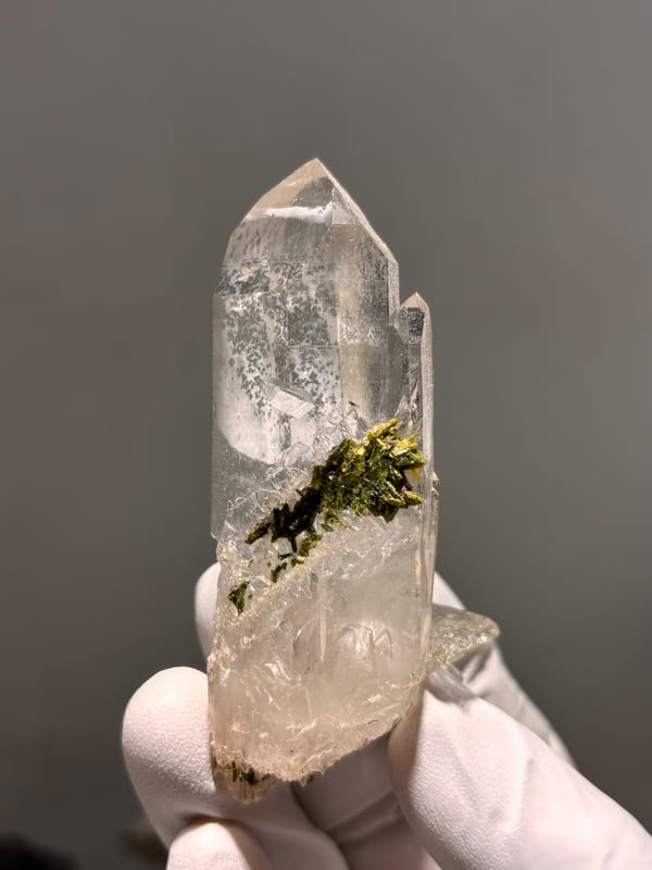 Clear quartz point with green epidote inclusion from Sichuan, China, held in gloved hand