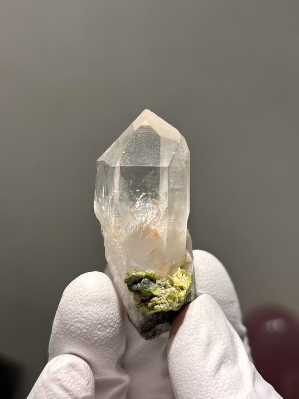 Clear quartz point on green epidote base from Sichuan, China, held in gloved hand