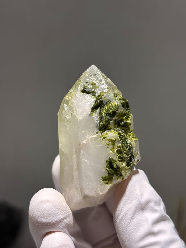 Milky quartz point with green epidote on its face from Sichuan, China, held in gloved hand