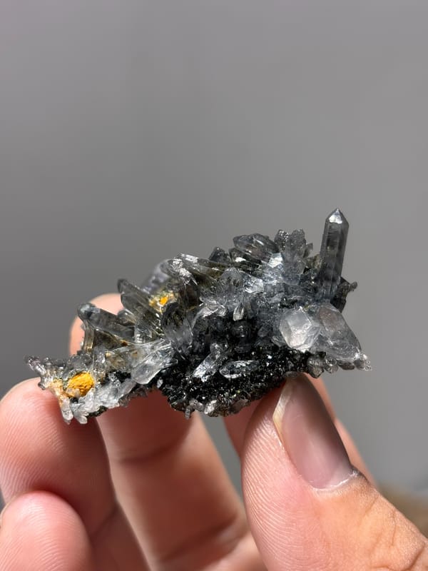 Grey quartz cluster with epidote and orange flecks from Yunnan, China, held in hand