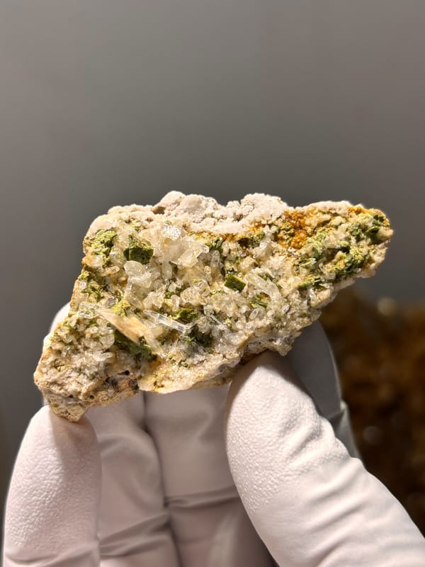 Green epidote in quartz-feldspar slab from Meigu, Sichuan, China, held in gloved hand