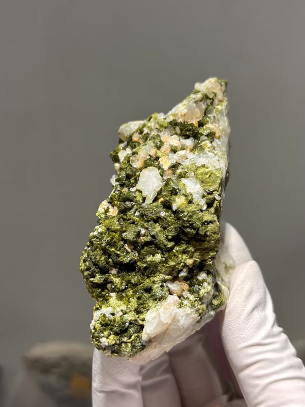 Block of green epidote with white quartz from Sichuan, China, held in gloved hand