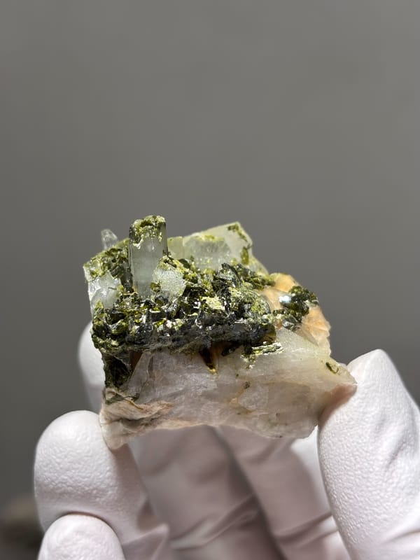 Green epidote with clear quartz on white matrix from Sichuan, China, held in gloved hand