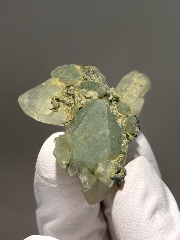Pale green epidote-tinted quartz points from Sichuan, China, held in gloved hand