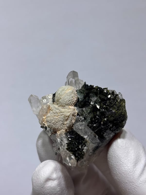 Pale green prehnite ball with quartz and dark epidote from Yunnan, China, held in gloved hand