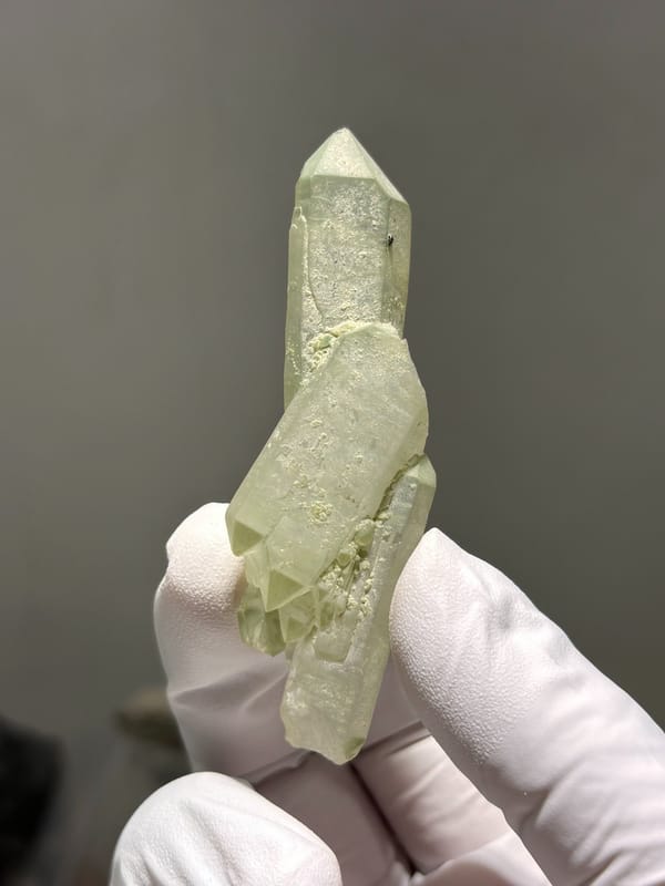 Pale green epidote-tinted quartz wand from Sichuan, China, held in gloved hand