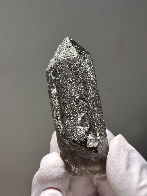 Dark smoky quartz point with mica-dusted tip from Fujian, China, detail of the matrix contact