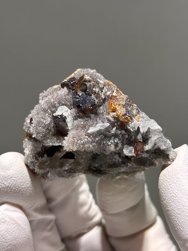 Dark red-brown sphalerite crystals on grey quartz from Hubei, China, held in gloved hand